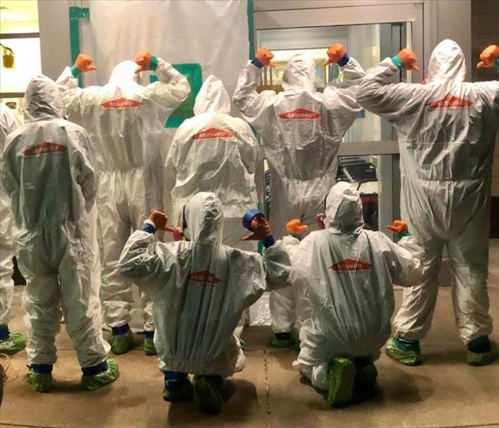 image of 8 SERVPRO workers from the back pointing at the SERVPRO logo on their PPE suits