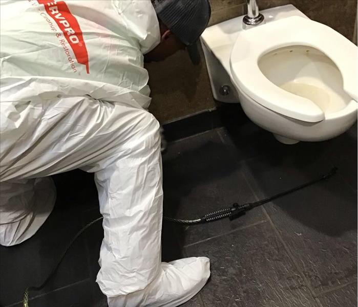 photo of SERVPRO worker wearing PPE finishing a commercial bathroom overflow job  
